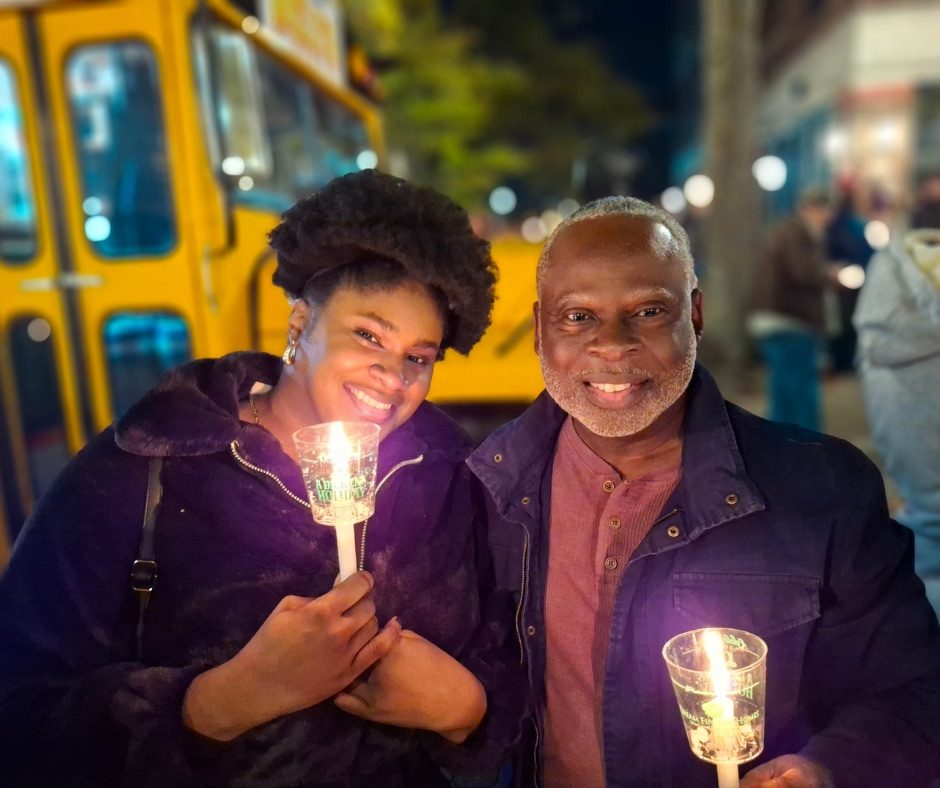 A couple smiling together while holding candles at A Dickens Holiday